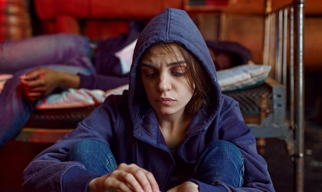 A young person captured sitting next to bed, contemplating to use drugs