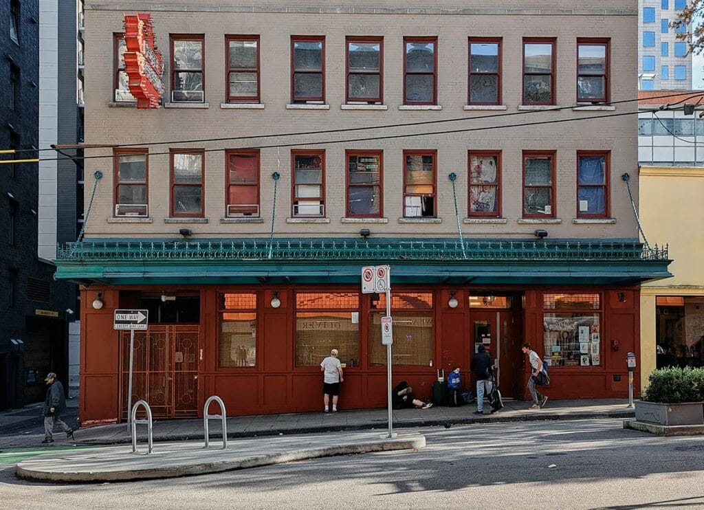People are captured on a sidewalk in front of the Hotel Canada SRO in Downtown Vancouver