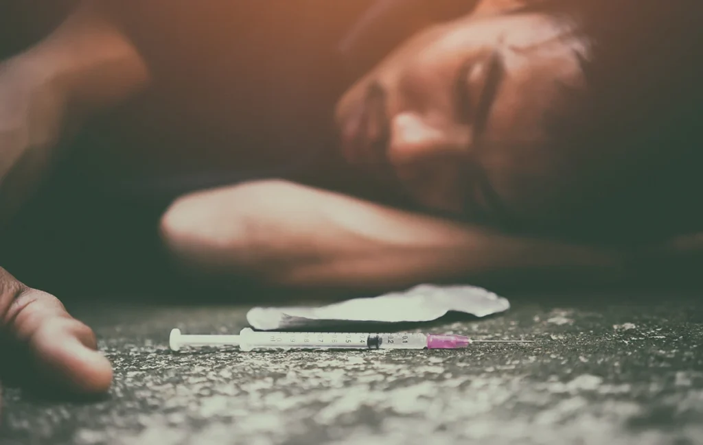 An image of an overdose victim lying on the ground next to a syringe