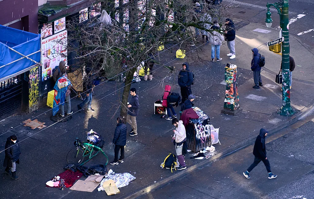 An aerial view of people gathering on a busy street corner in Vancouver's Downtown Eastside, showcasing street activity and daily life against an urban backdrop.