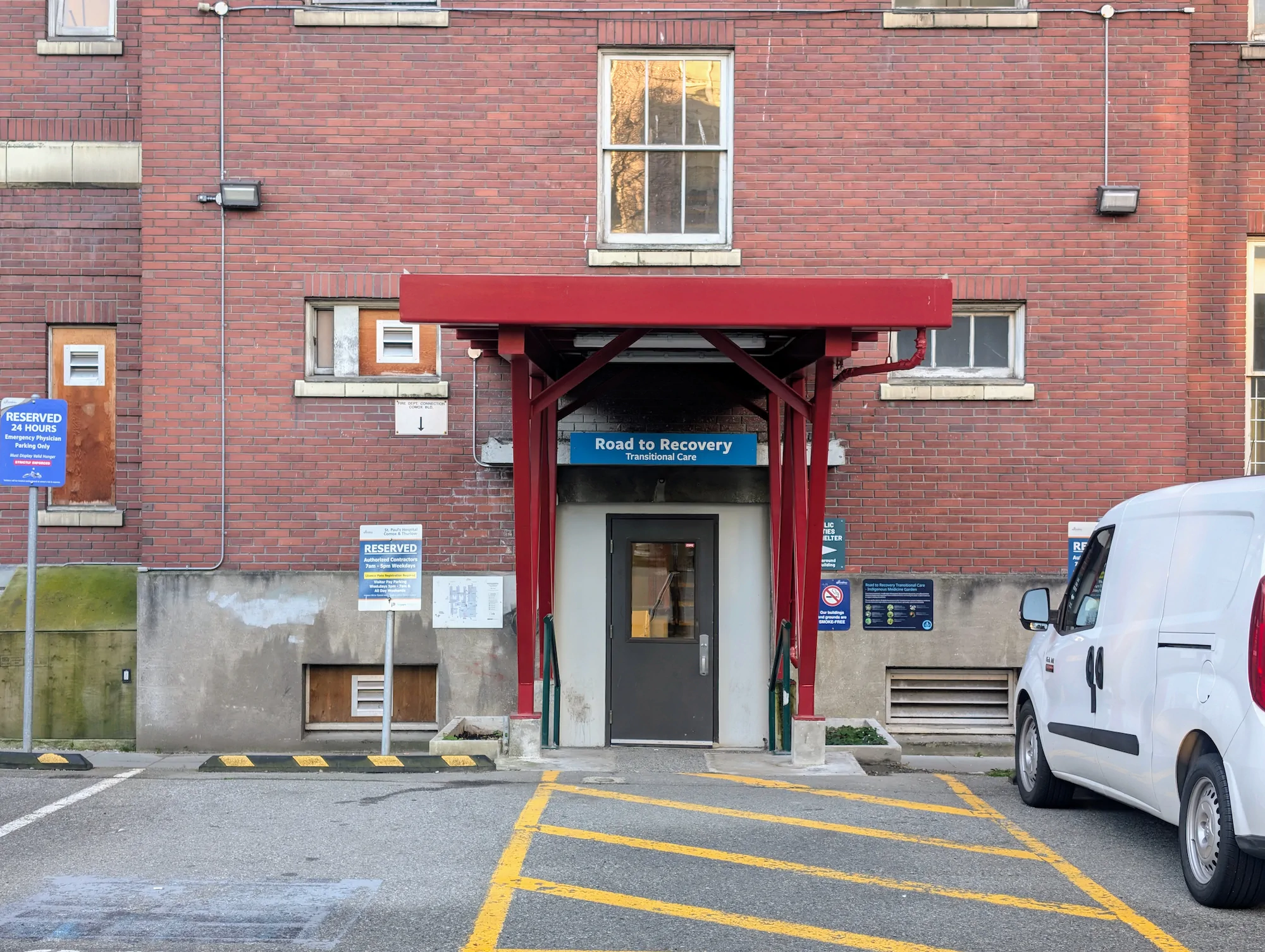 Red awning framing the entrance to the Road to Recovery Transitional Care facility at a brick hospital building in Vancouver.