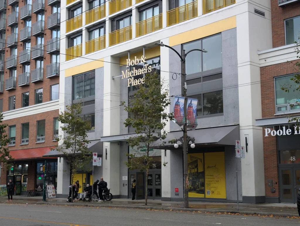 Exterior view of Bob & Michael's Place housing development at 58 West Hastings Street in Vancouver with pedestrians on the sidewalk.
