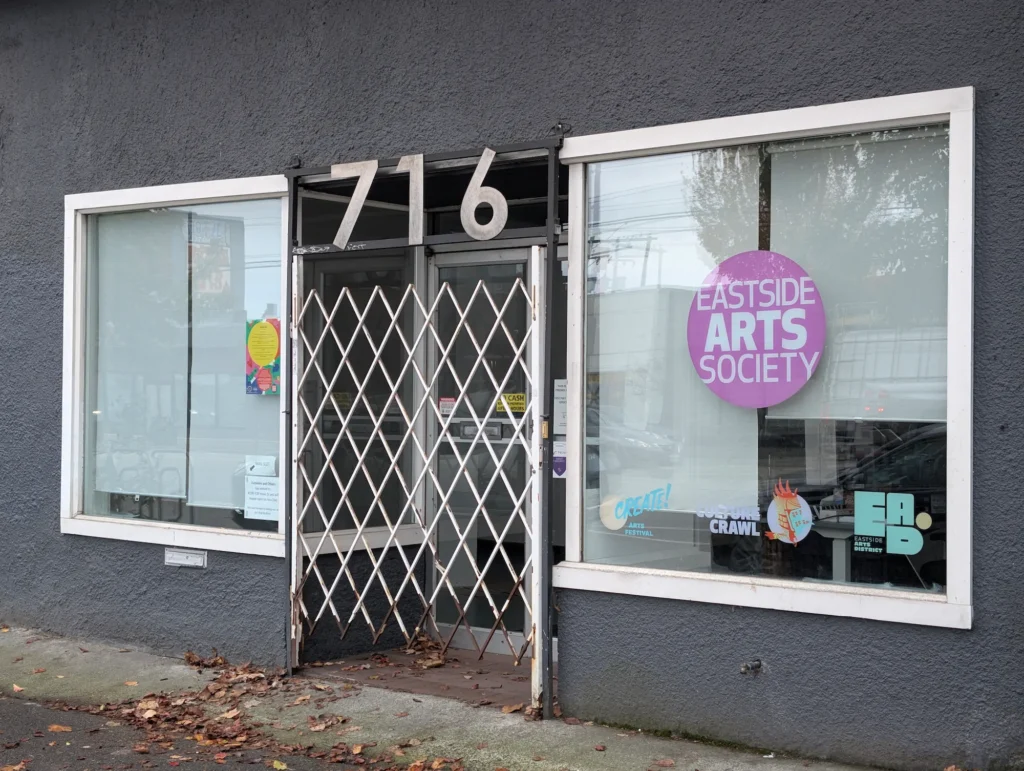 Exterior storefront at 716 East Hastings Street in Vancouver showing Eastside Arts Society and Culture Crawl window signage behind a metal entry gate.
