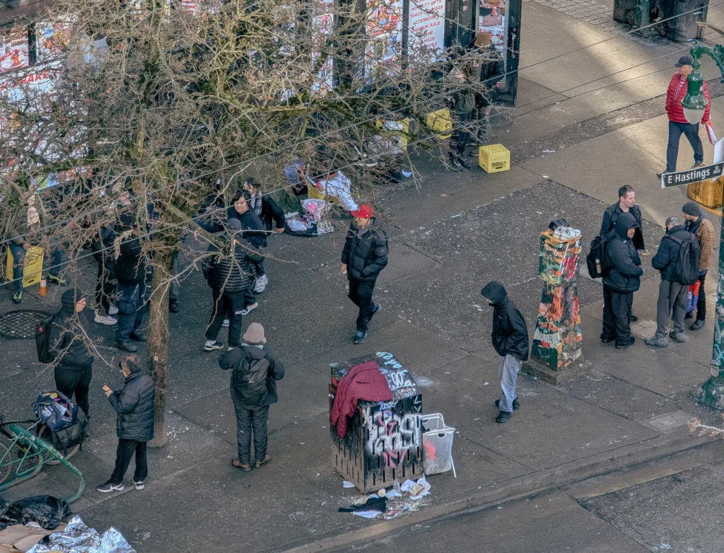 High-angle overhead view of people gathering and walking along an East Hastings Street sidewalk in Vancouver's Downtown Eastside.