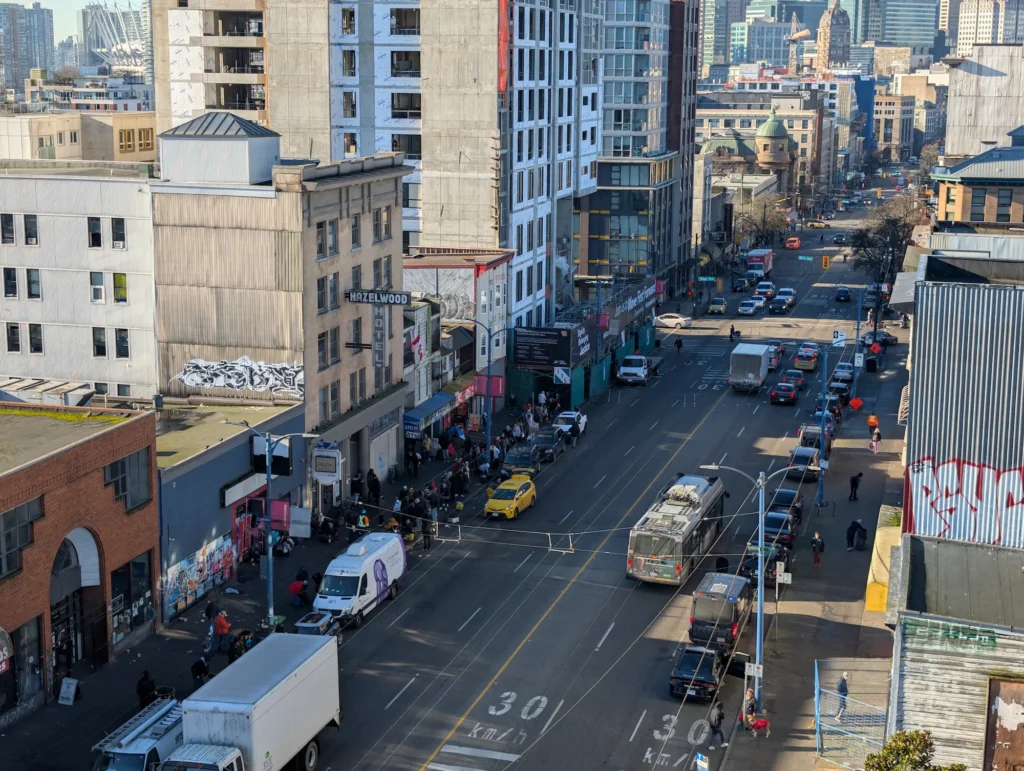 Elevated view looking down East Hastings Street in Vancouver's Downtown Eastside showing sidewalk crowds, traffic, and historic buildings.