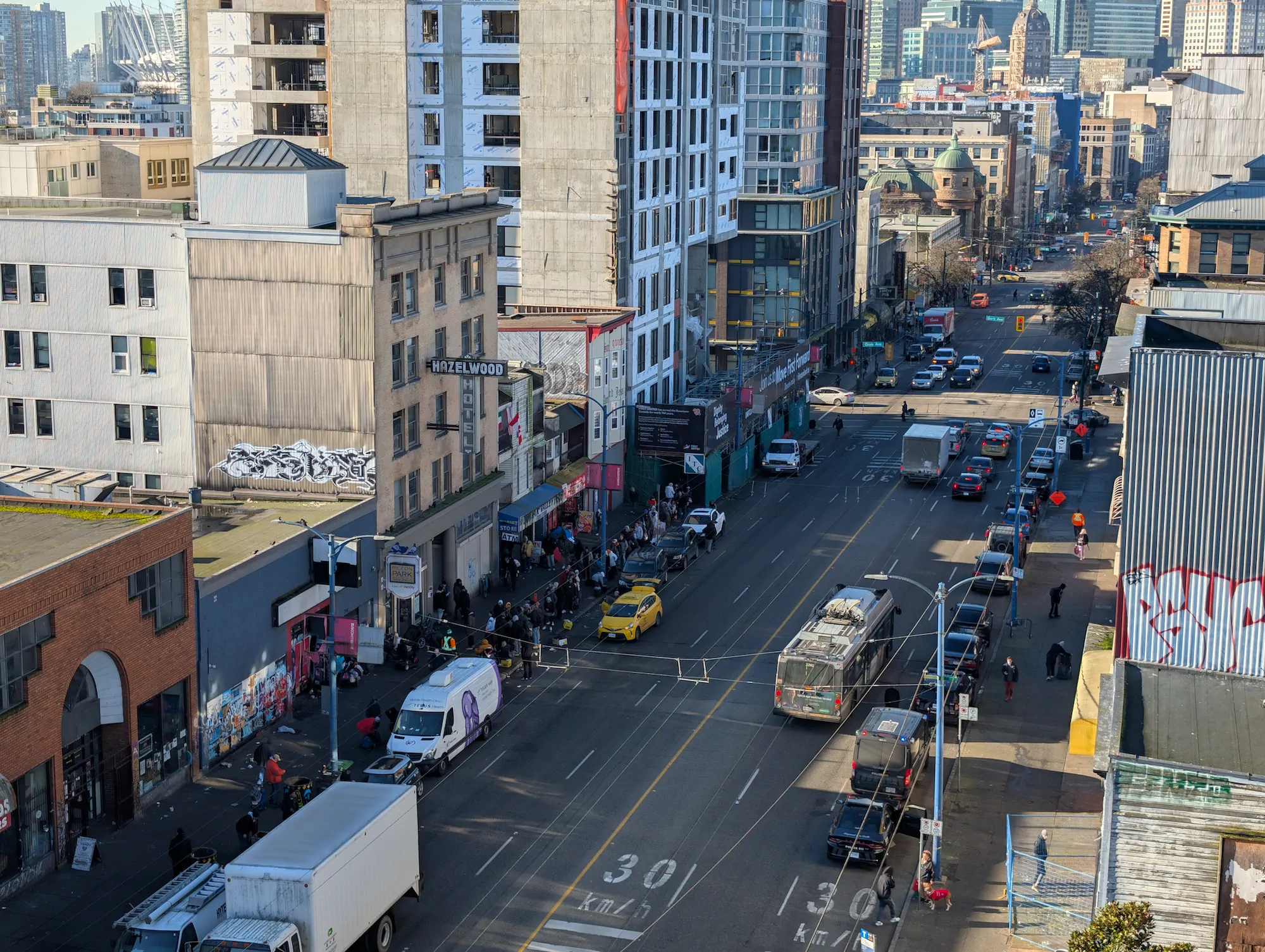 Elevated view looking down East Hastings Street in Vancouver's Downtown Eastside showing sidewalk crowds, traffic, and historic buildings.